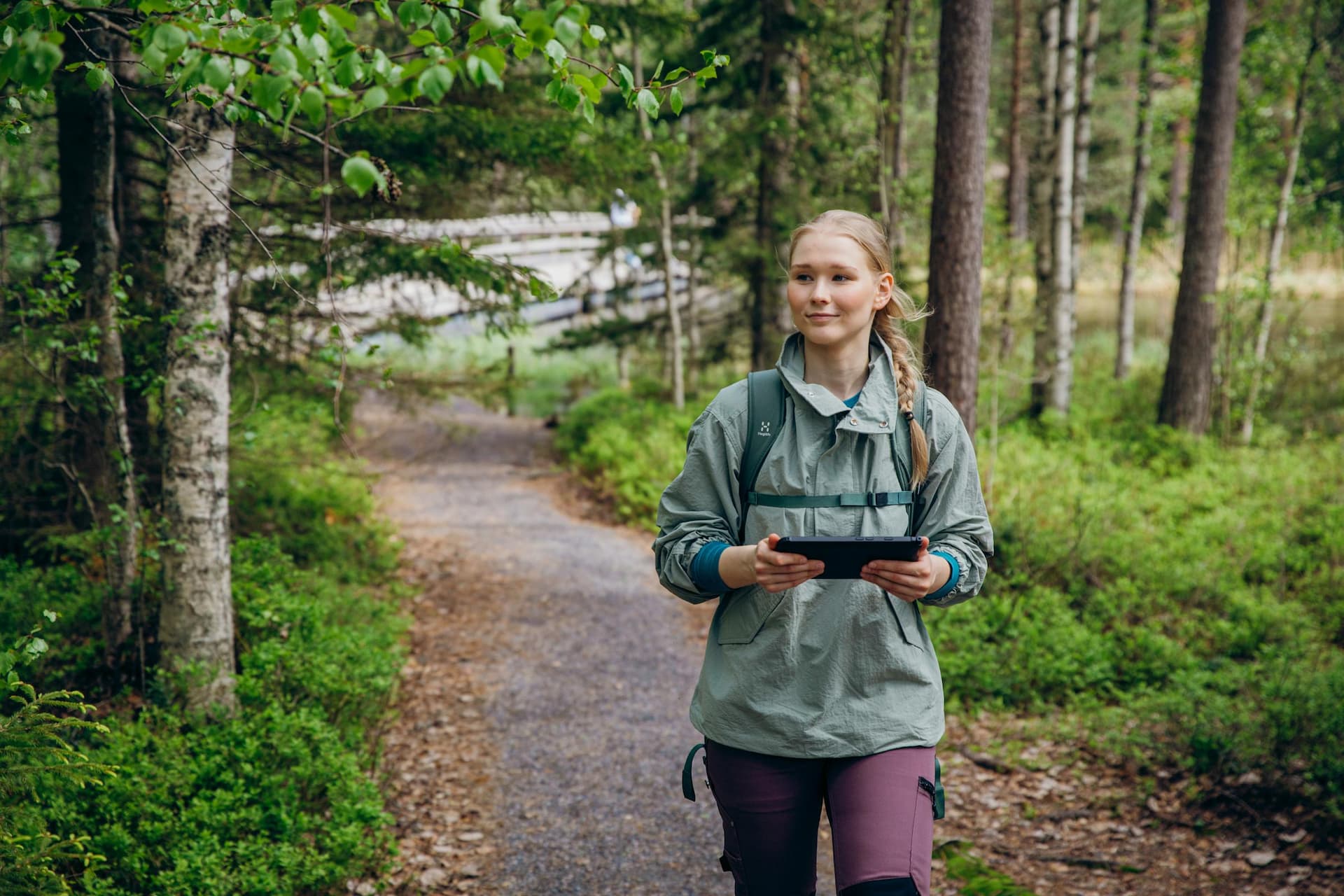 RFI brand photoshoot in Espoo, Finland. Environmental Specialist walking in outdoor clothing in a forest with an iPad in Nuuksio National Park, Finland.