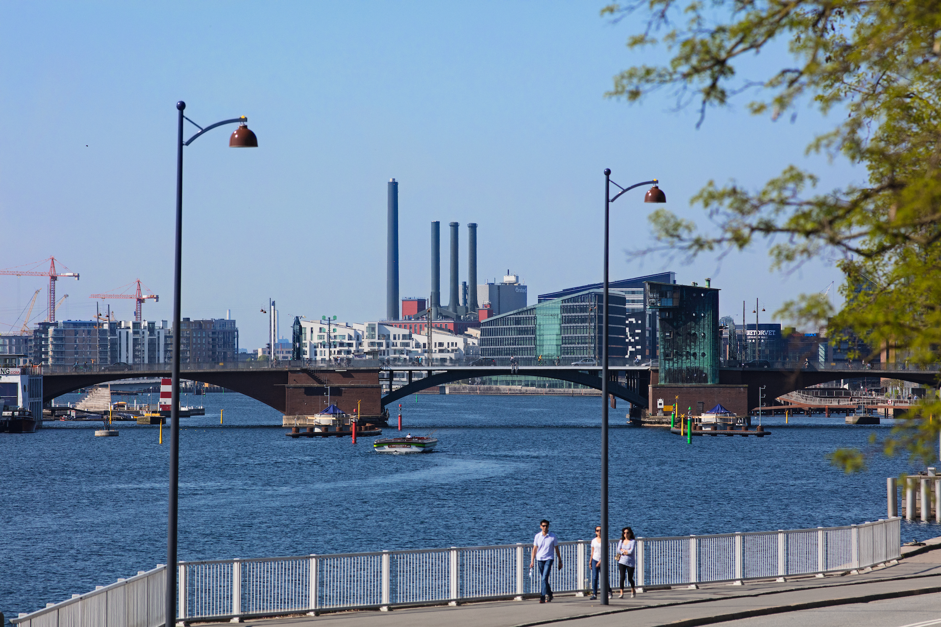 people walking in front of Copenhagen bridge and harbour bath with industry facility in background