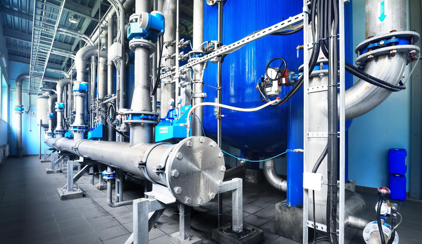 Large industrial water treatment and boiler room. Shiny steel metal pipes and blue pumps and valves.